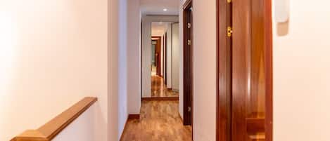 A hallway with wooden flooring, a wooden door on the right, and a staircase on the left.