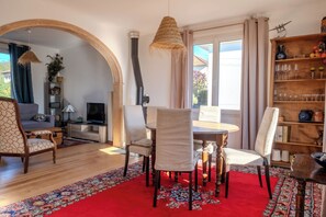 A living room with a fireplace, a dining table with chairs, a TV, and a bookshelf. - Cozy house in Figeac (46100), garden, 2 bedrooms, sleeps 4. 🌳 (Figeac)