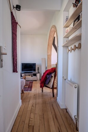 A narrow hallway with wooden flooring, a television, a bed with a red blanket, and a radiator. - Cozy house in Figeac (46100), garden, 2 bedrooms, sleeps 4. 🌳 (Figeac)
