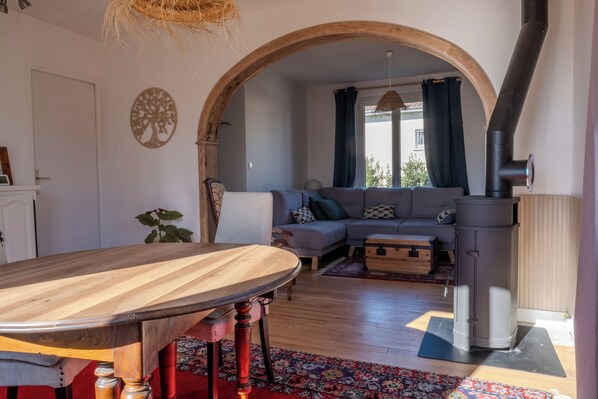 A living room with a wooden dining table, a sofa, a fireplace, and a large window with curtains.
