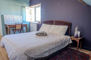 A bedroom with a bed, a desk, a chair, a radiator, a window, a star decoration, and a nightstand with a vase. - Cozy house in Figeac (46100), garden, 2 bedrooms, sleeps 4. 🌳 (Figeac)