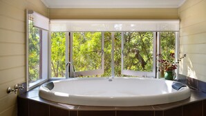 Ein Badezimmer mit einer großen Badewanne, einem Fenster mit Blick auf Bäume und einem Topf mit einer Pflanze auf dem Fensterbrett.