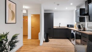 A modern kitchen with a wooden floor, black cabinets, a microwave, and a washing machine. - City Point Aberdeen by Guestz (Aberdeen)