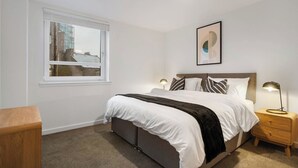 A bedroom with a bed, bedside tables, a window, and a wall-mounted picture. - City Point Aberdeen by Guestz (Aberdeen)