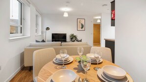 A dining area with a round table set for four, a sofa in the background, and a television on a stand. - City Point Aberdeen by Guestz (Aberdeen)