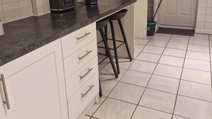 Una cocina con armarios blancos, una encimera negra, un tostador, una cafetera y una escoba apoyada en la pared.