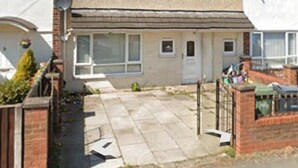 Una casa residencial de dos pisos con un jardín delantero, una antena parabólica y un portón de garaje visible.