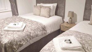 Una habitación doble con dos camas, una mesita de noche con lámpara, un cuadro en la pared y una ventana con cortinas.