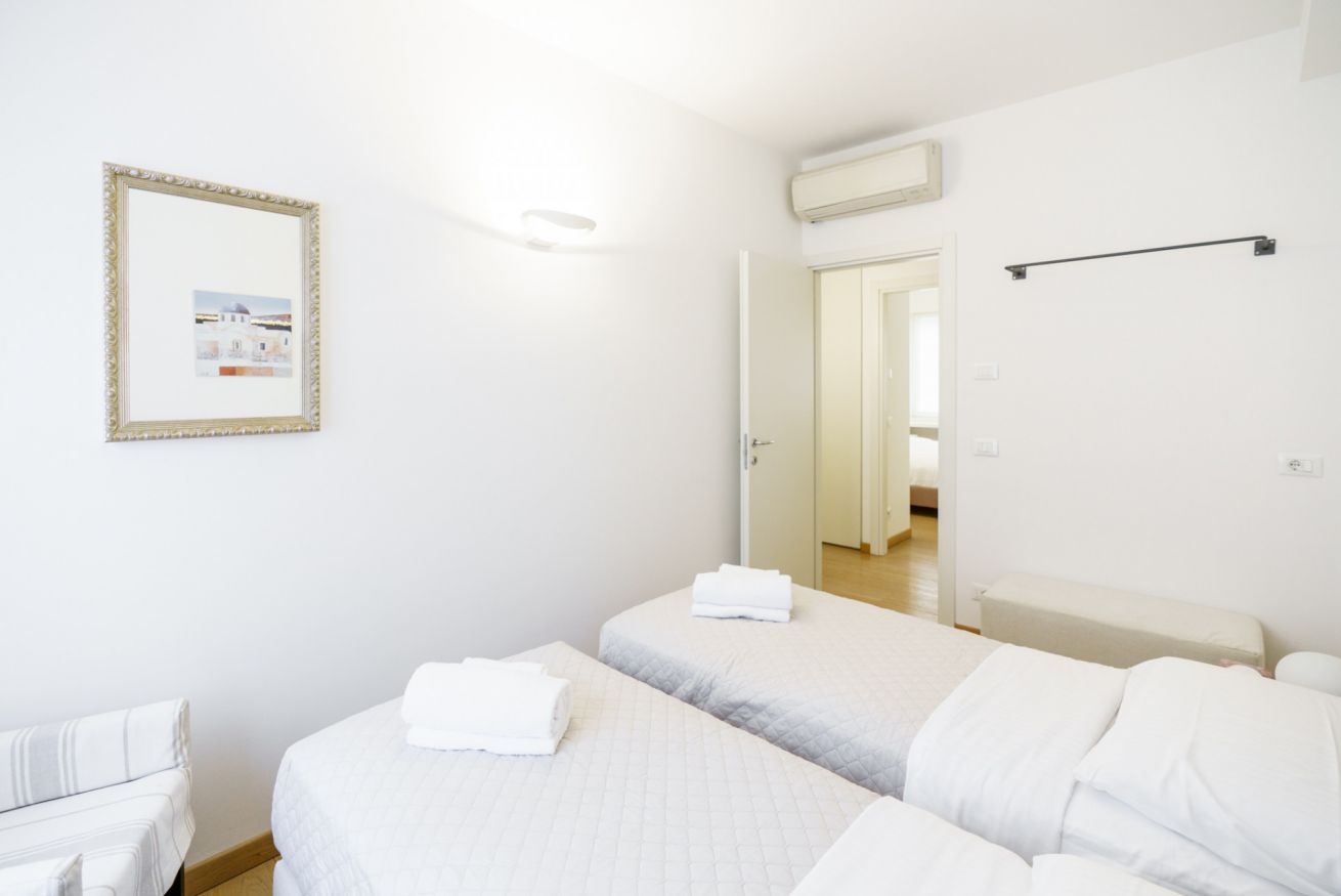 A hotel room with two beds, a white wall, a framed picture, and a door leading to another room.