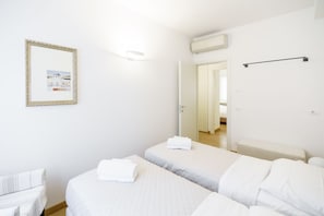 Une chambre d’hôtel avec deux lits, un mur blanc, un tableau encadré et une porte donnant sur une autre pièce.