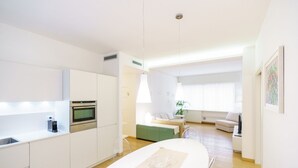 A modern kitchen with white cabinetry, a built-in oven, and a dining area with a white table and chairs. - Cozy and central Vicolo Stella residence (Verona)