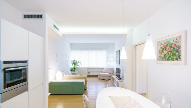 A modern kitchen with built-in appliances, a dining area with a table and chairs, and a living space with a sofa and a television. - Cozy and central Vicolo Stella residence (Verona)
