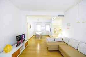 Ein modernes Wohnzimmer mit einer Couch, einem Fernseher und einem Essbereich mit Tisch und Stühlen.