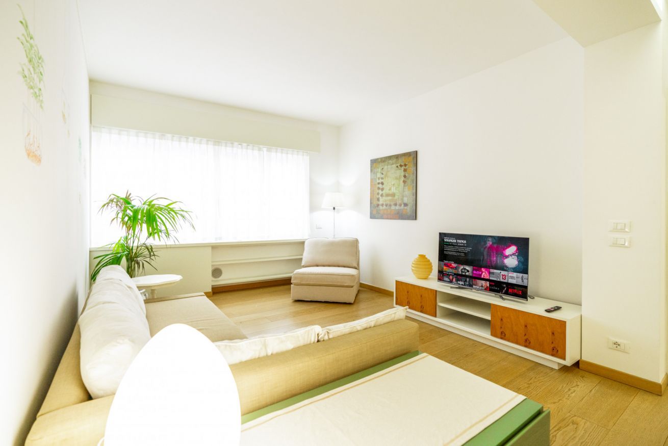 Een moderne woonkamer met een bank, een televisie, een lamp en een plant.