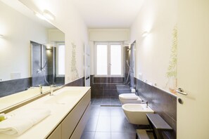 Uma casa de banho moderna com um espelho grande, duas lavatórios, uma banheira e uma sanita.