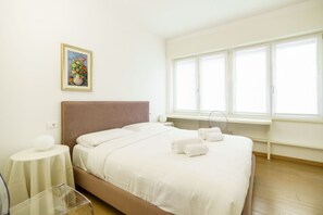 Quarto de hotel com cama, mesa de cabeceira, janela com persianas e um quadro na parede.