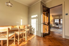 A dining area with wooden furniture, a kitchen with white cabinets, and a view of a living room through an open door. - South Castle Street | St Andrews (St Andrews)
