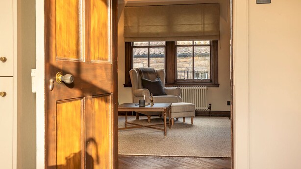 A room with a wooden door, a window with a view, a chair, a table, and a radiator. - South Castle Street | St Andrews (St Andrews)