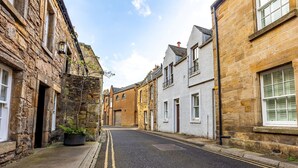 A narrow street lined with historic stone buildings, a clear sky, and a double yellow line on the road. - South Castle Street | St Andrews (St Andrews)
