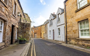 A narrow street lined with historic stone buildings, a clear sky, and a double yellow line on the road. - South Castle Street | St Andrews (St Andrews)