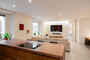 Eine moderne Küche mit Kochinsel, Essbereich mit Sofa und flach an der Wand befestigtem Bildschirm.