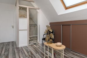 A room with a sloped ceiling, a staircase leading to an upper level, a chair with a decorative plant, and a small table with a bowl.