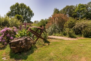 A garden with a rustic wooden bench, a metal sculpture, and various plants. - Cottage “La Tour de Merlin” with Private Terrace, Garden, and Wi-Fi (Plumelin)