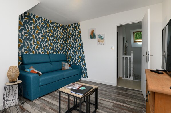 Un salon avec un canapé bleu, une petite table basse en bois et un mur orné d’un motif.
