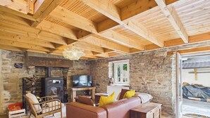 A cozy living room with a stone wall, wooden ceiling beams, a fireplace, a sofa, and a television. - ROCA - Charming farmhouse (La Forêt-Fouesnant)