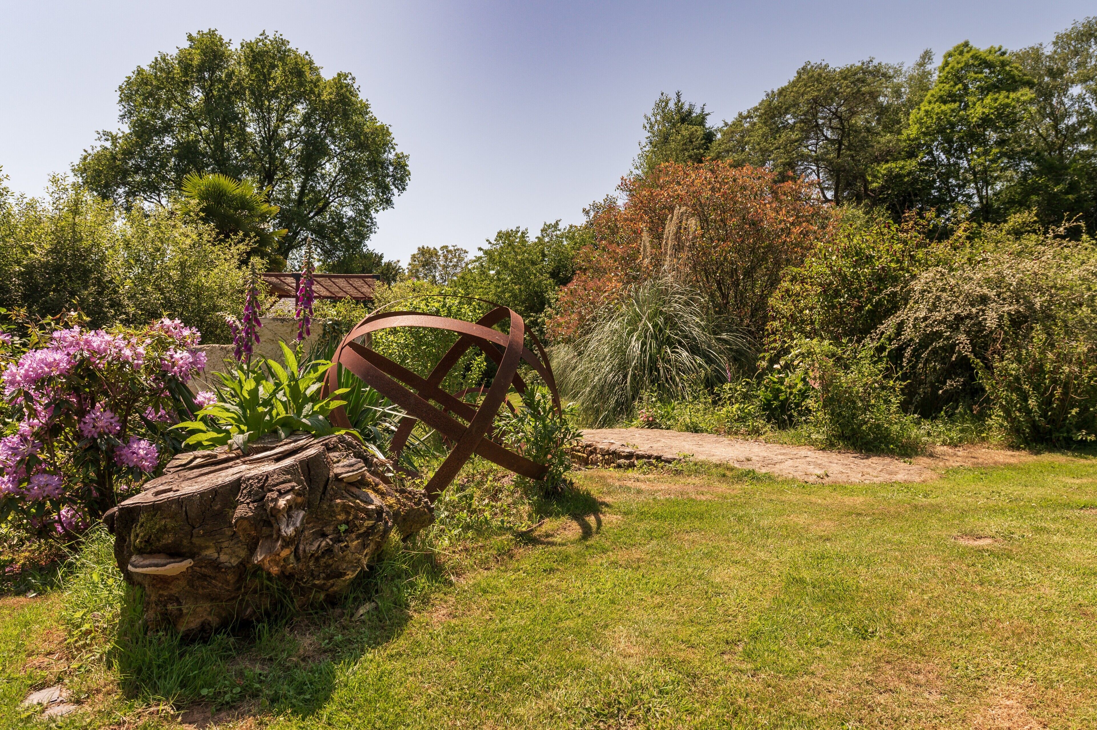 Un jardin agrémenté d’une sculpture en bois, d’un banc en pierre et de diverses plantes.