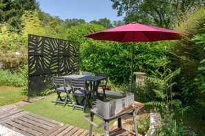 A patio with a table and chairs, a grill, and a red umbrella. - Cottage "Le Nid de Tristan et Iseut" with Private Terrace, Garden, and Wi-Fi (Plumelin)