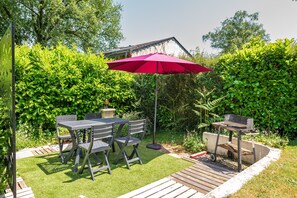 A patio with a table and chairs, a grill, and a red umbrella.