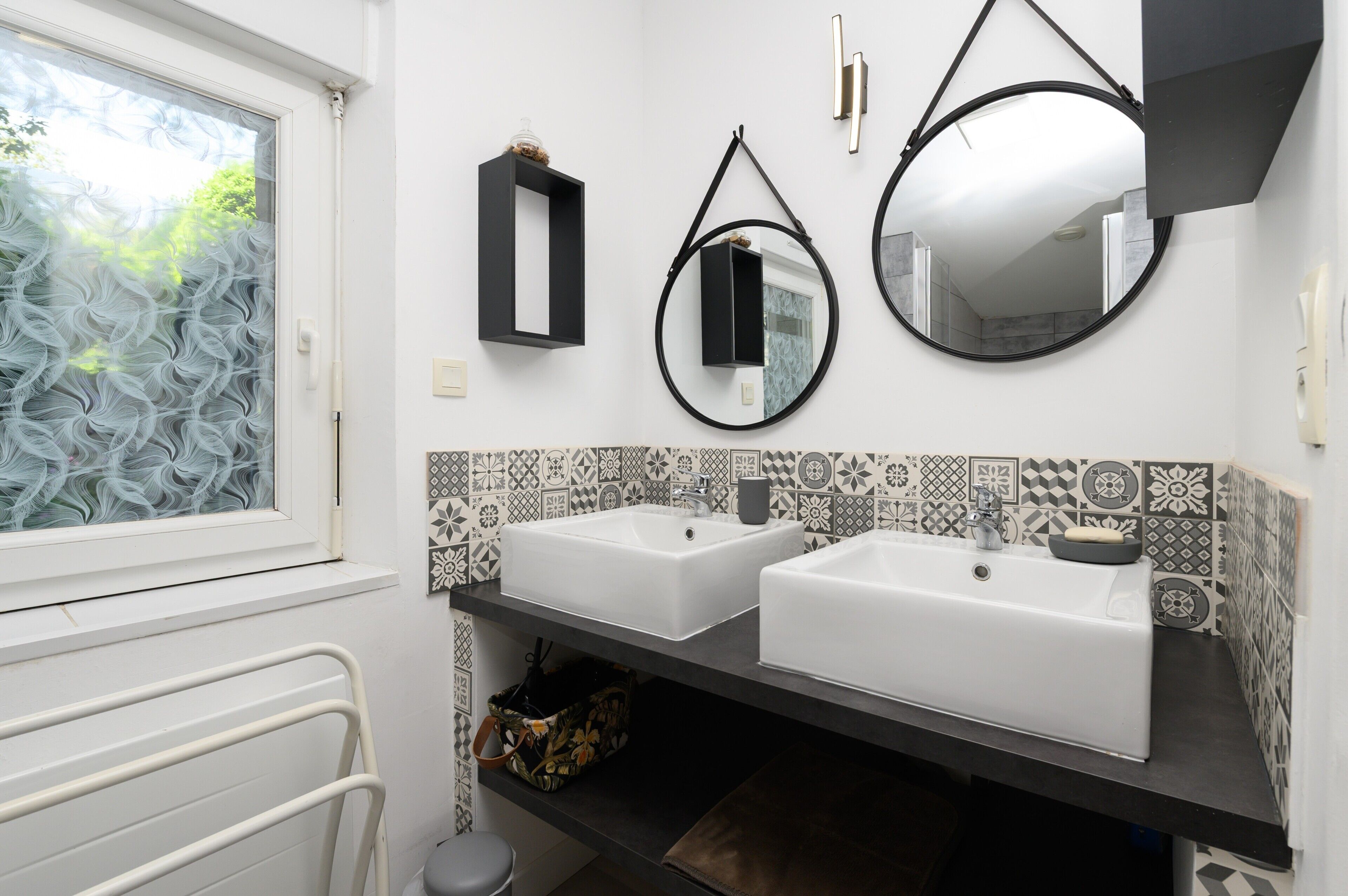 A bathroom with two sinks, a window, a towel rack, and a mirror.
