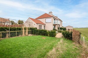 A two-story house with a red-tiled roof, a visible balcony, and a well-maintained lawn. - The Wee Holm | St Andrews (Kincaple)