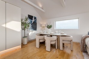 A dining area with a wooden table, four chairs, a potted plant, a lamp, and a window. - The Wee Holm | St Andrews (Kincaple)