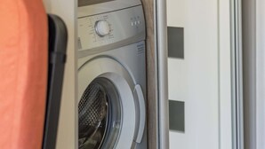 Ein kompakter, moderner Waschraum mit integrierter Waschmaschine und Trockner, einer Schiebetür und Holzboden.