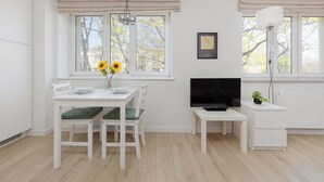 Ein modernes Zimmer mit Esstisch, Stühlen, Fernseher und kleinem Schreibtisch.