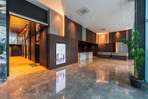 A modern lobby with a polished marble floor, wooden paneling, and a reception desk.