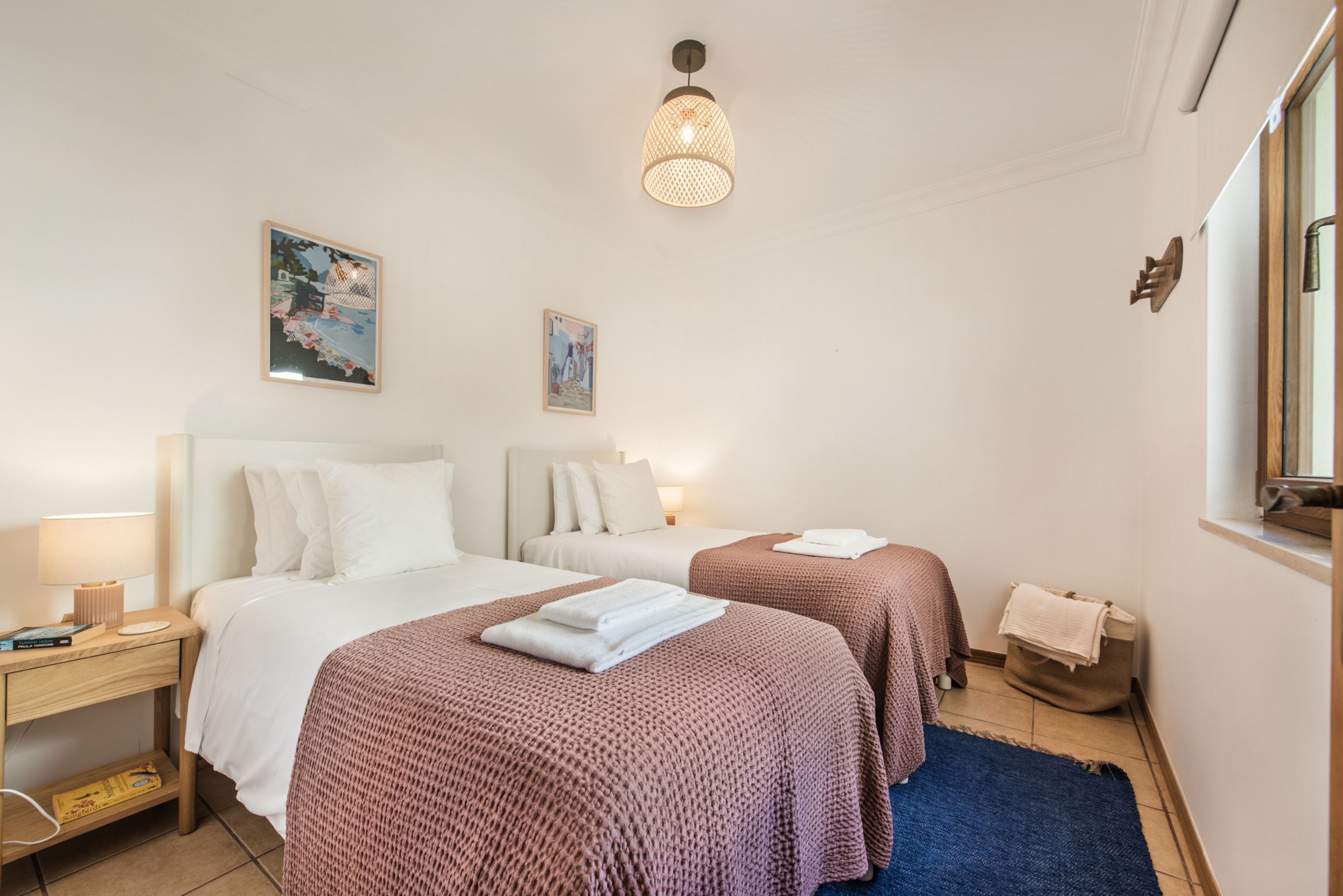 Habitación de hotel con dos camas, una mesita de noche, una lámpara, una lámpara colgante y una alfombra azul.