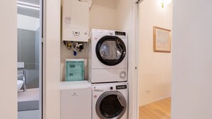 Ein Waschraum mit einer übereinander gestapelten Waschmaschine und einem Trockner, einem Putzschrank und einem gerahmten Bild an der Wand.