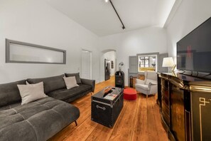 A modern living room with a sofa, a red ottoman, a black cabinet, and a television. - 1 BR Apartment in Neubau, 8 min city center, AC (Wien)