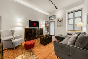 A living room with a grey sofa, a red ottoman, a dark wooden cabinet, a flat-screen TV, and a bookshelf. - 1 BR Apartment in Neubau, 8 min city center, AC (Wien)