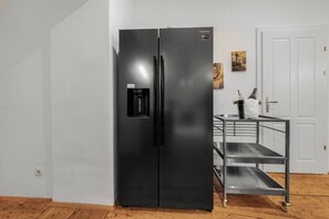 A black refrigerator with a water dispenser, a white door, and a metal cart with shelves. - 1 BR Apartment in Neubau, 8 min city center, AC (Wien)