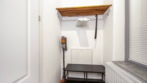 Et aflangt rum med en hvid dør, en radiator, en sort hylde og en ventil i loftet.
