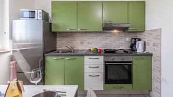 A compact kitchen with green cabinets, a stainless steel refrigerator, a microwave, a stove, and a coffee maker.