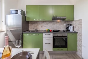 A compact kitchen with green cabinets, a stainless steel refrigerator, a microwave, a stove, and a coffee maker.
