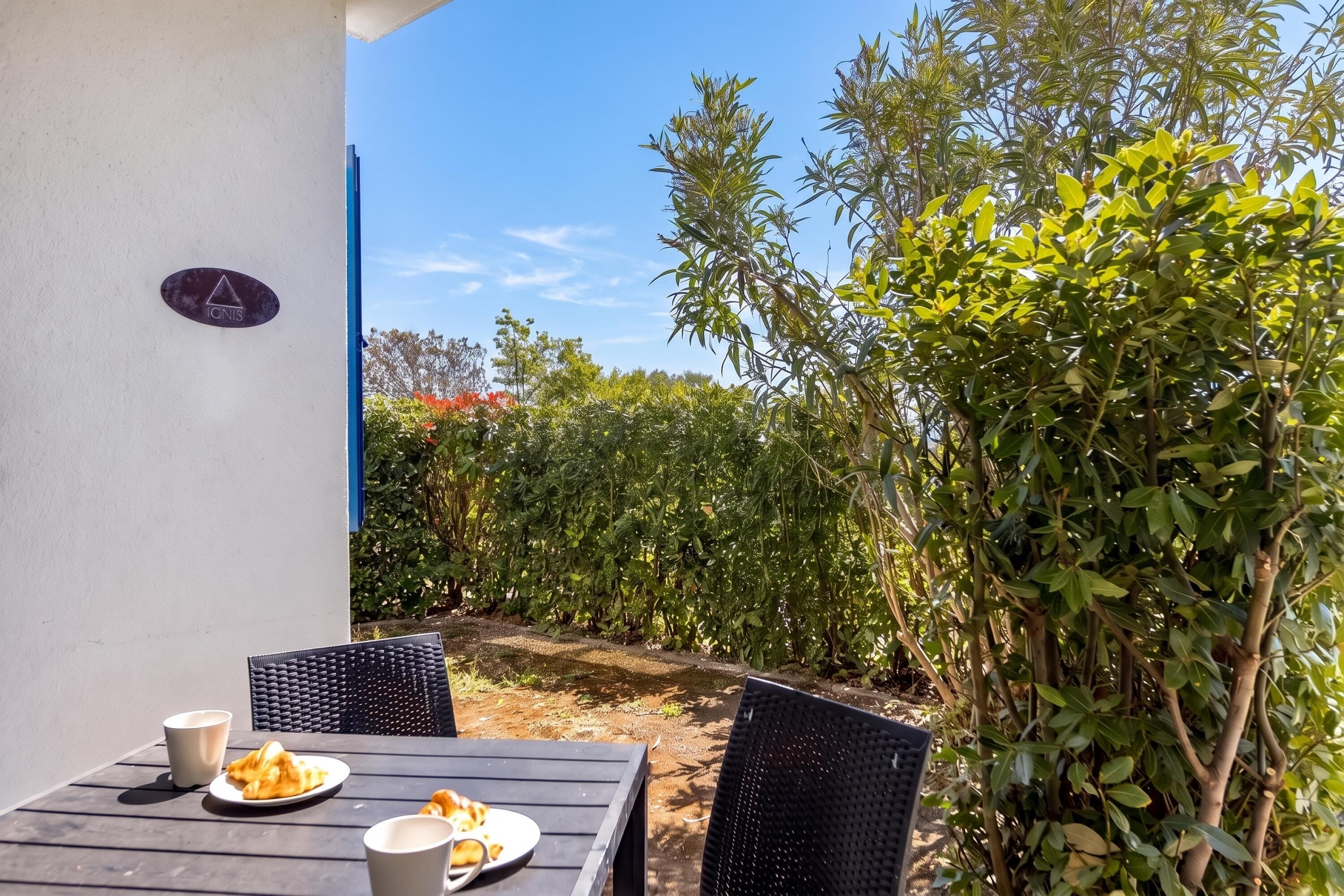 Un área de comedor al aire libre con una mesa y sillas, un letrero en la pared y un seto al fondo.