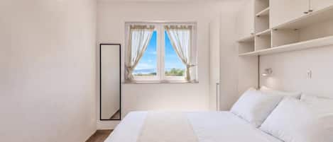 A bedroom with a bed, a window with curtains, a mirror, and built-in shelving.