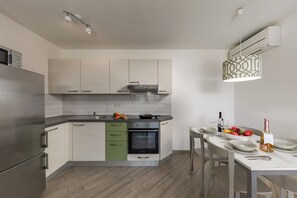 A modern kitchen with a built-in oven, a dining table set for two, and a hanging light fixture. - Wabi Sabi Apartments With Pool (Krk)