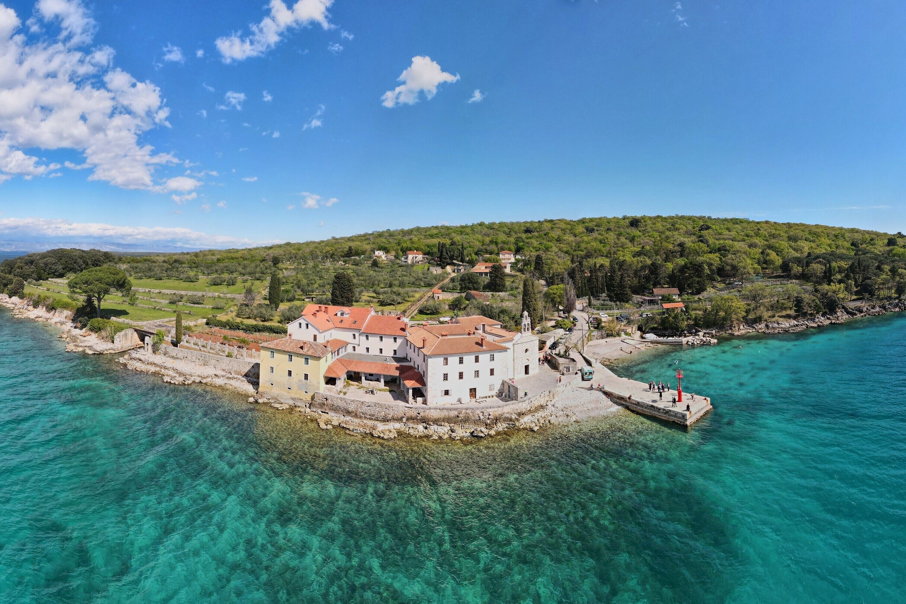 Un pueblo costero con edificios cerca del agua, un muelle y una colina al fondo.